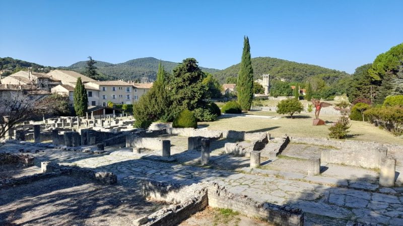 vue du site antique de la Vilasse avec des habitations sur le côté gauche et des arbres et des collines au fond et à droite